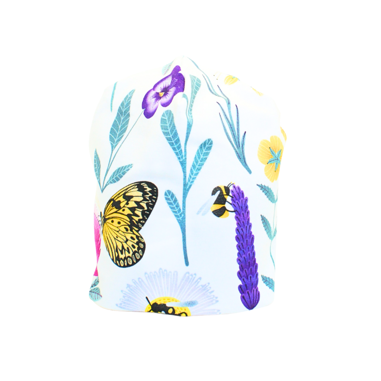 Vit trikåmössa med mönster av färgglada blommor och insekter i lila, rosa, turkos och gult. Sydd i dubbel ekologisk trikå.