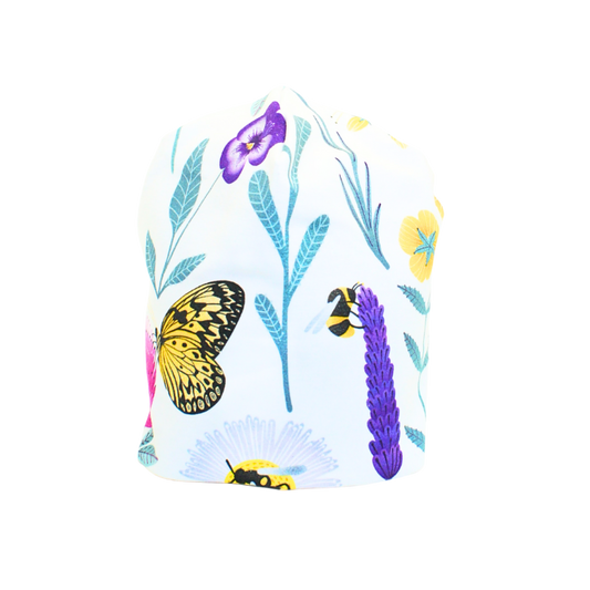 Vit trikåmössa med mönster av färgglada blommor och insekter i lila, rosa, turkos och gult. Sydd i dubbel ekologisk trikå.